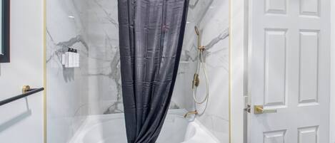 A modern bathroom with a glass-enclosed shower, a white bathtub, and a marble wall.