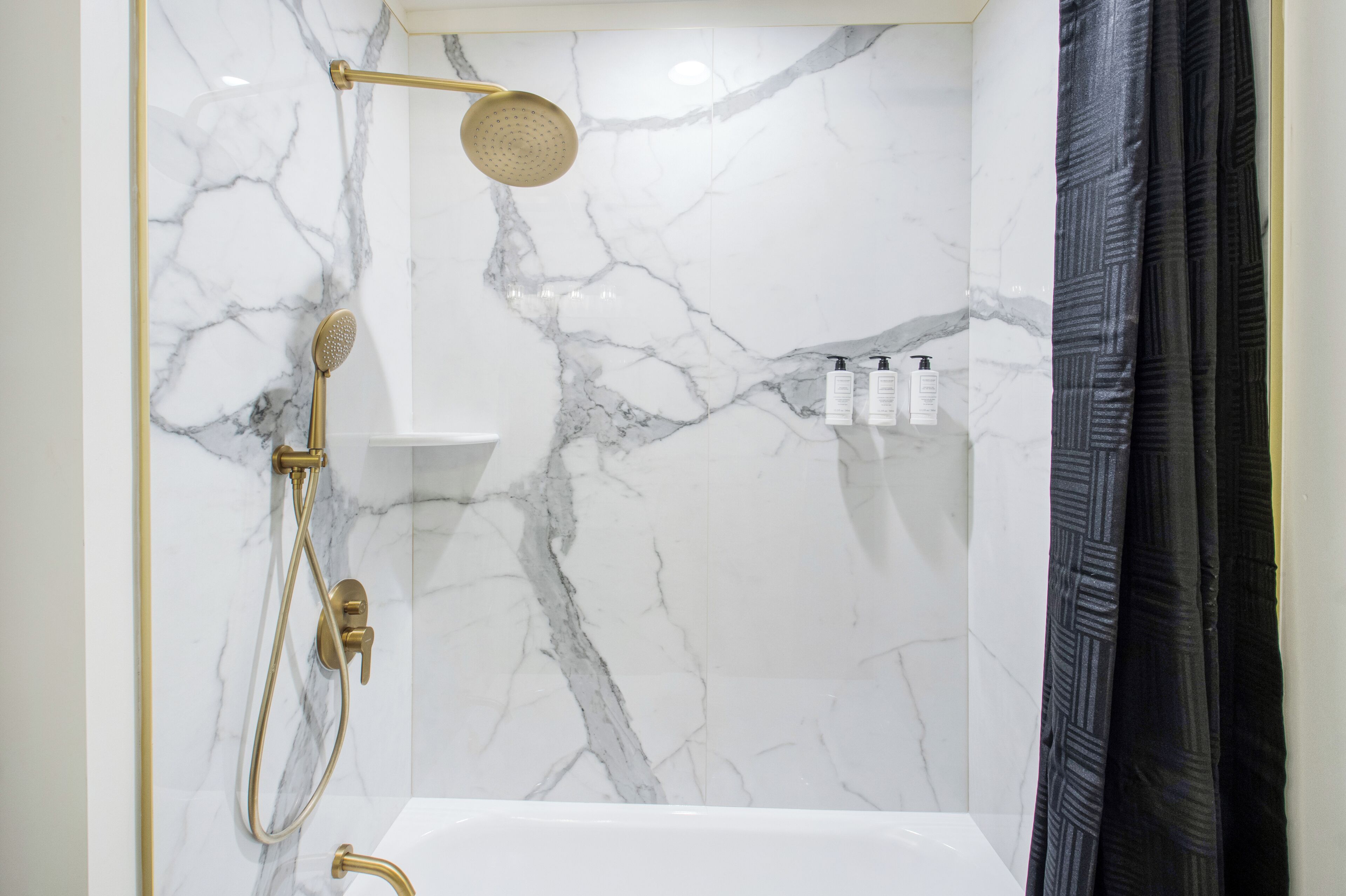 Ein Badezimmer mit Marmorwand, goldener Brause und Badewanne.