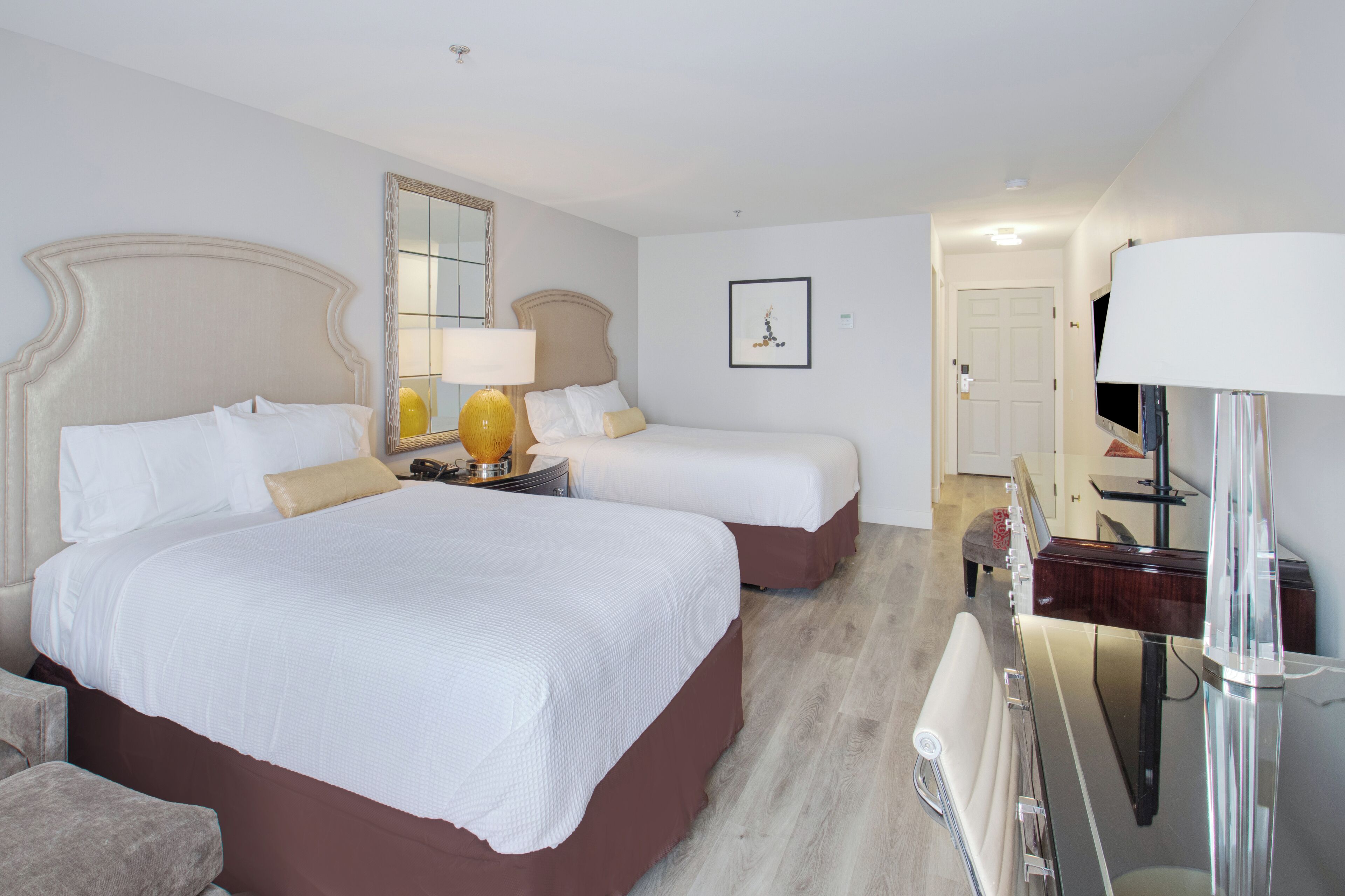 A hotel room with two beds, a large mirror, a television, and a bedside table with a lamp.