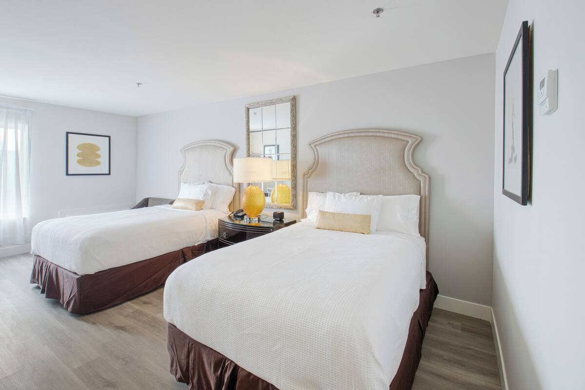 Quarto de hotel com duas camas, um espelho grande e uma mesa de cabeceira com luminárias.