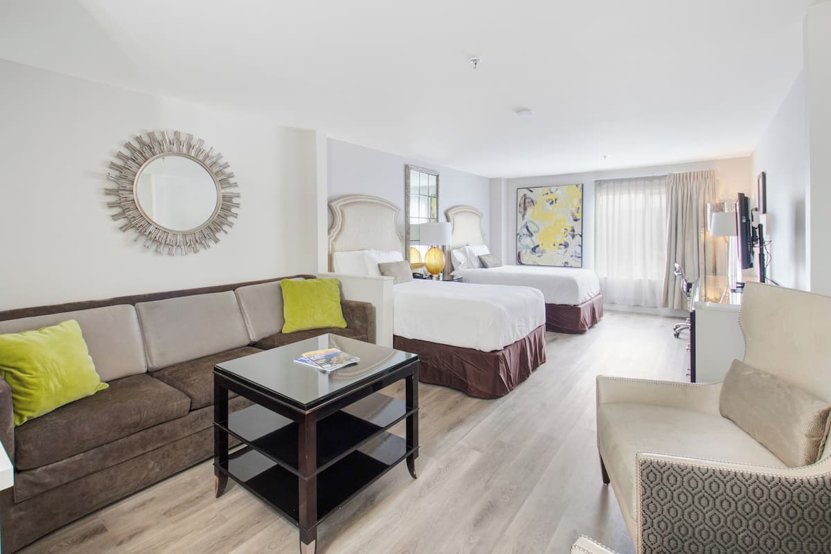 Quarto de hotel com sofá, mesa de centro, cama, cadeira e um espelho grande na parede.