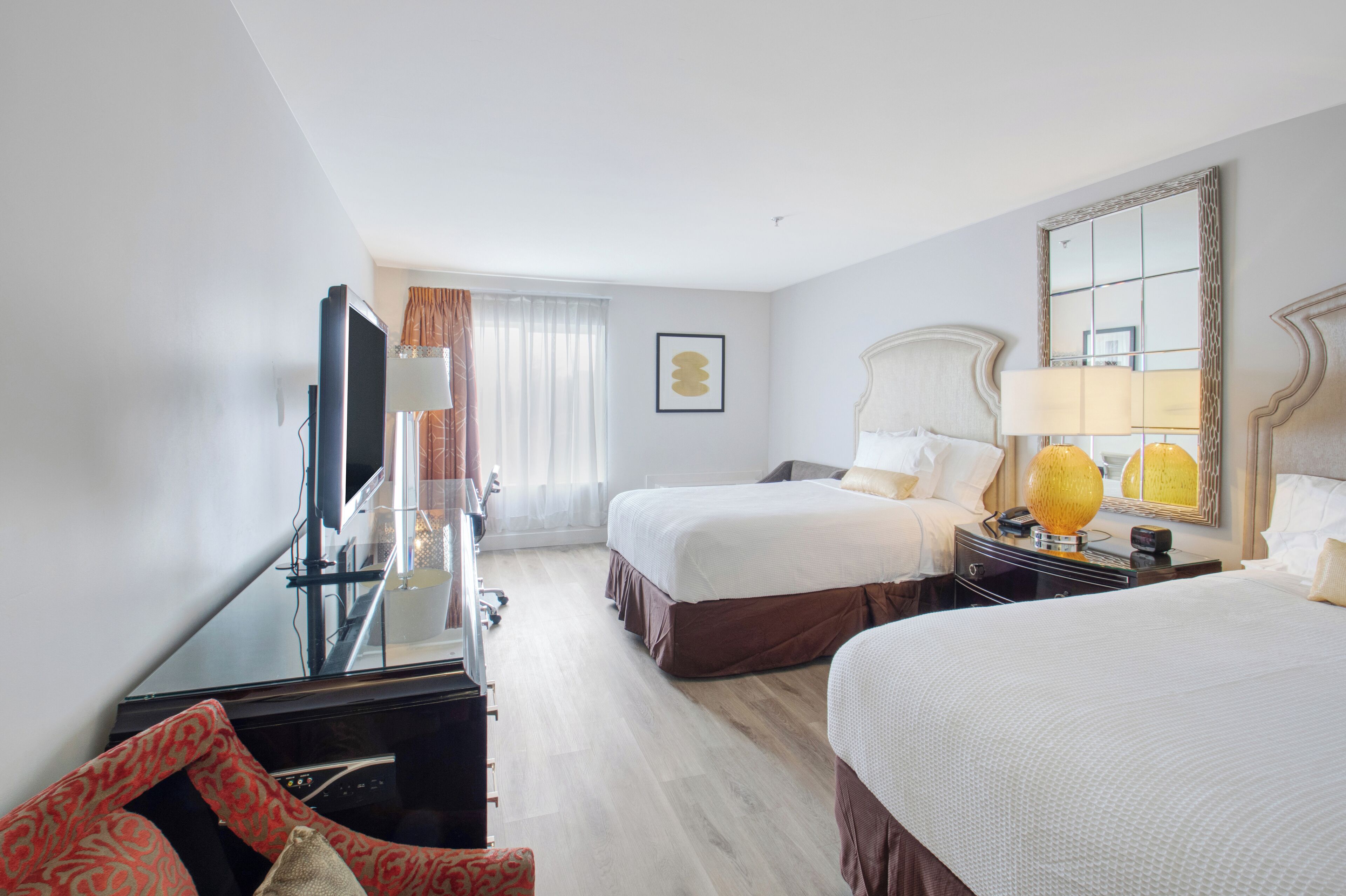 A hotel room with two beds, a desk, a TV, and a large mirror.