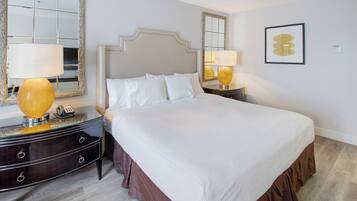A hotel room with a large bed, two bedside tables with lamps, a mirror, and a framed artwork on the wall.