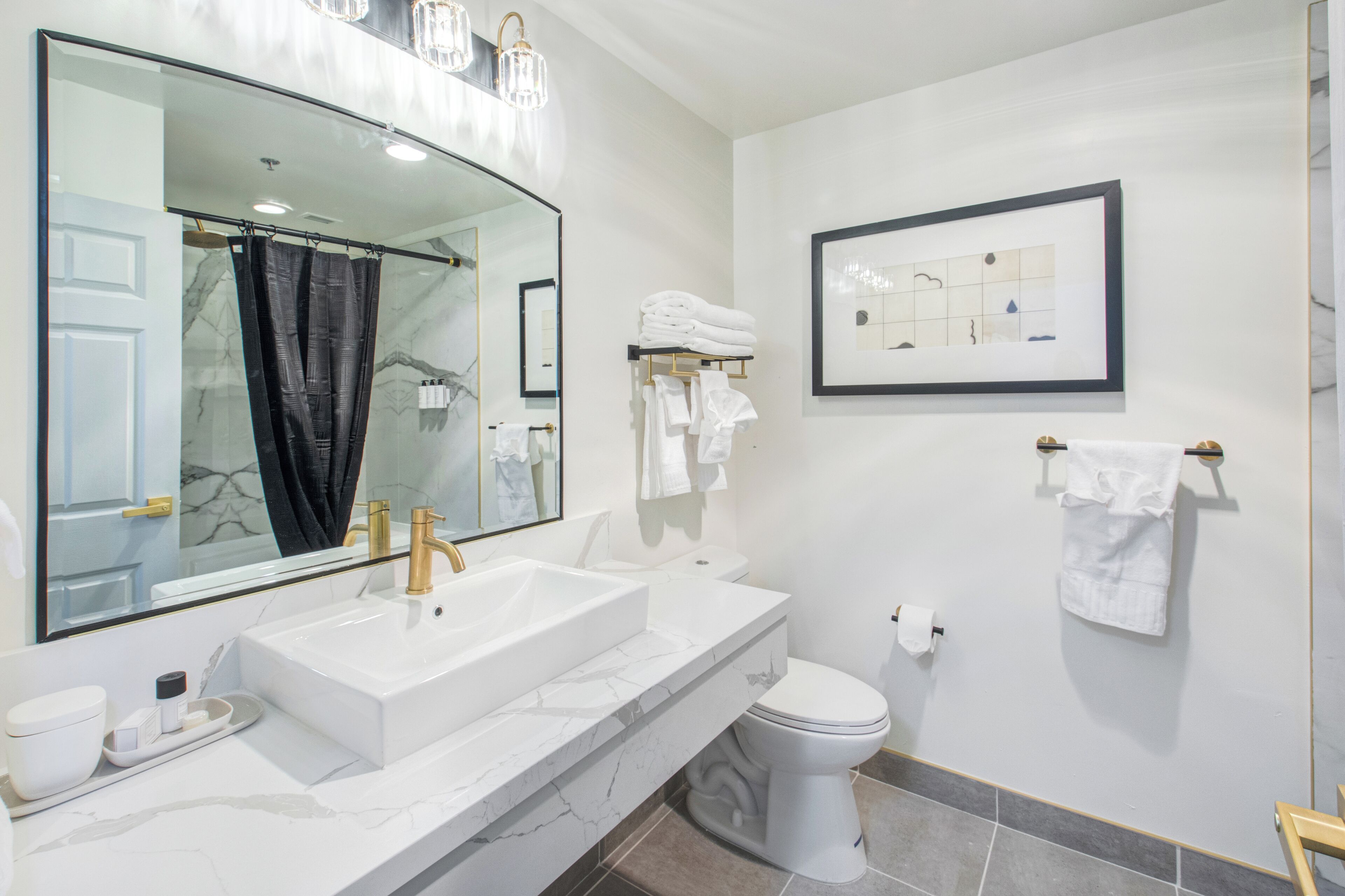 A modern bathroom with a large mirror, a white sink, a toilet, and a shower curtain.