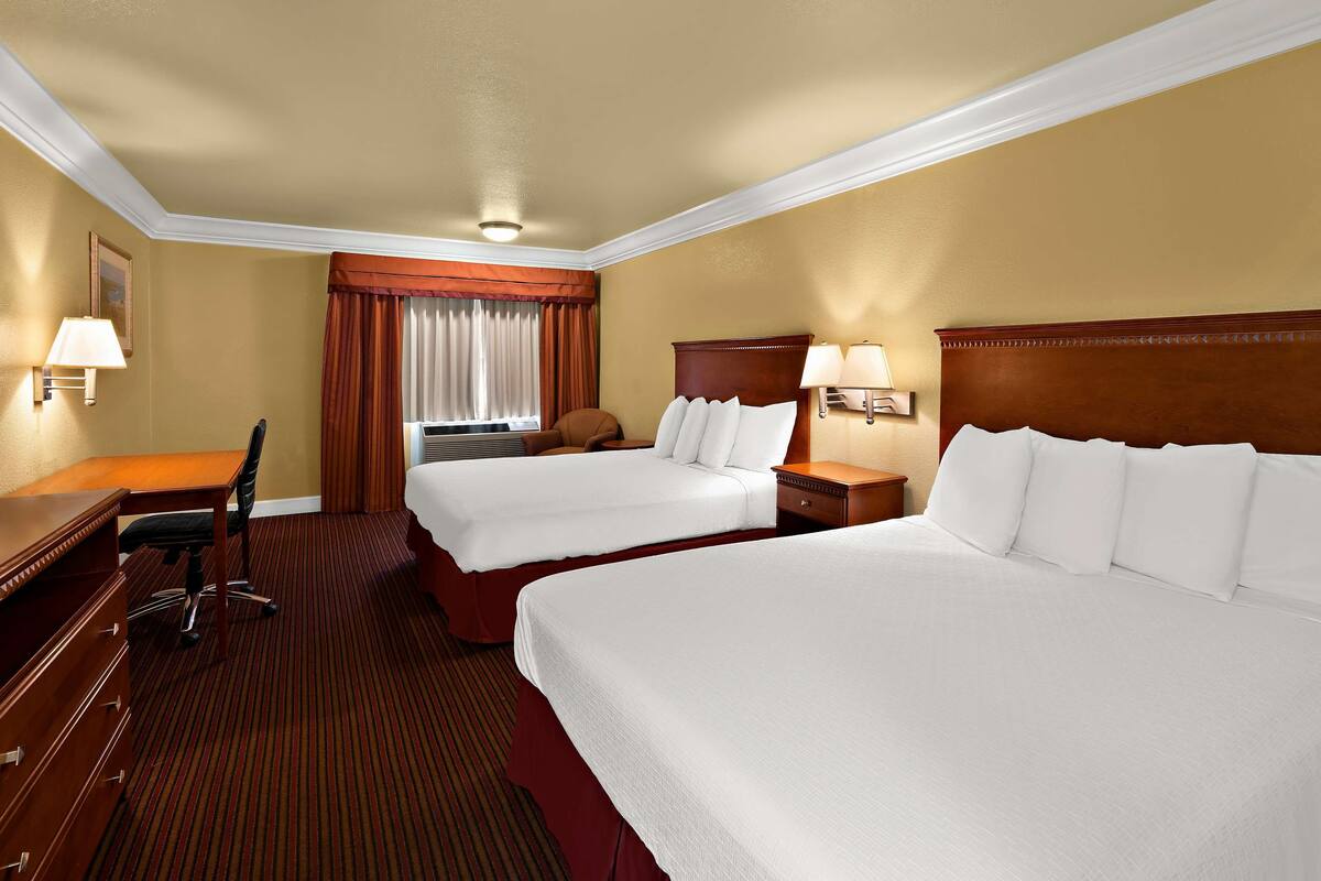 Quarto de hotel com duas camas, uma escrivaninha e uma cadeira.