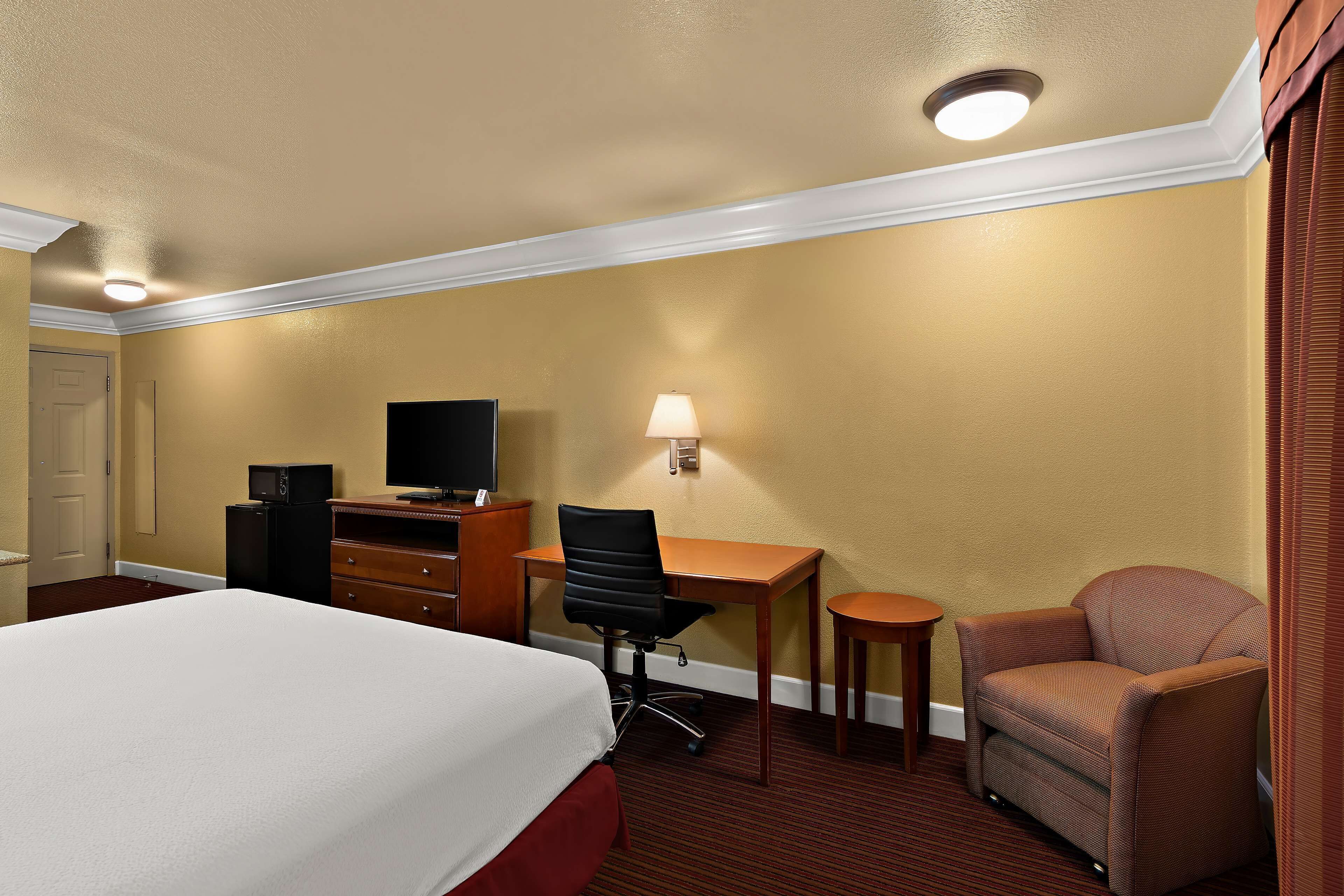 Ein Hotelzimmer mit Bett, Schreibtisch, Stuhl, Fernseher, Lampe und einem kleinen Tisch.