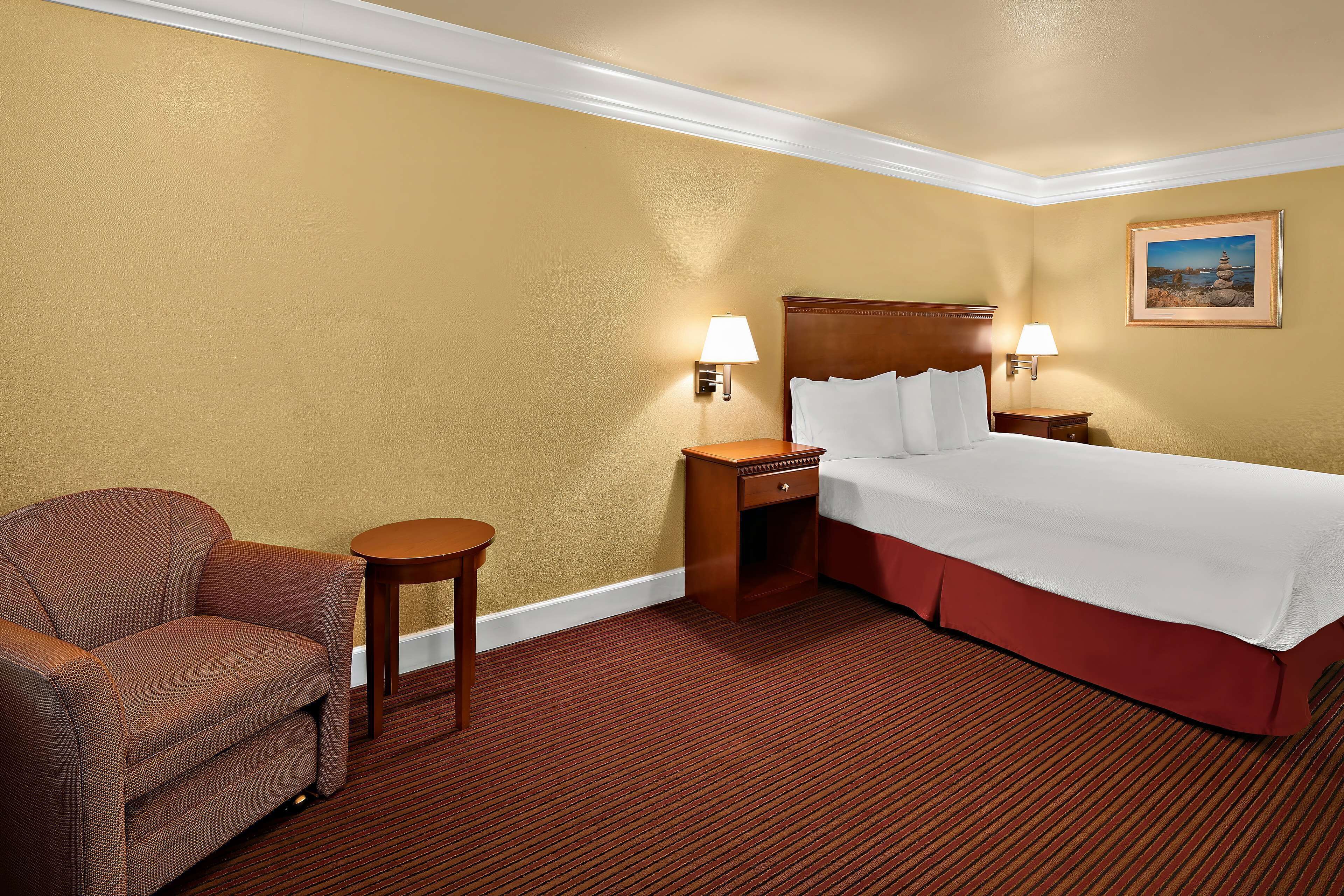 A hotel room with a bed, a chair, a nightstand, and a lamp.