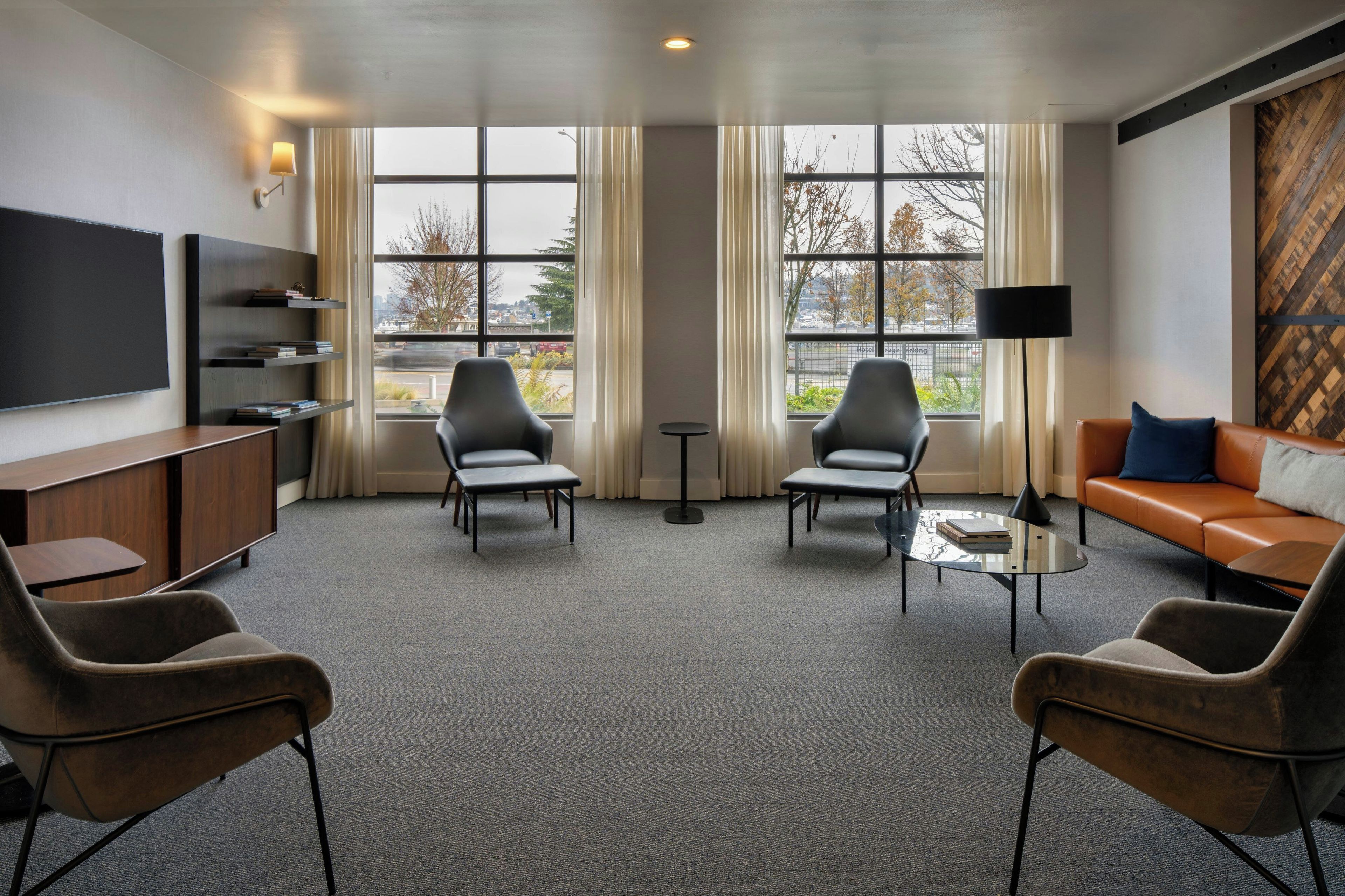 A modern hotel room with a flat-screen TV, a sofa, two armchairs, a coffee table, and a bookshelf.