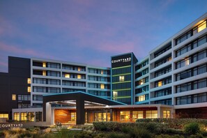 Un hotel moderno con varios pisos, una entrada destacada con zona cubierta y un letrero que indica que es un Courtyard by Marriott.