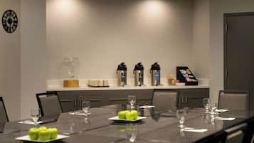 A conference room with a long table set for meetings, equipped with coffee makers, a water dispenser, and a clock on the wall.