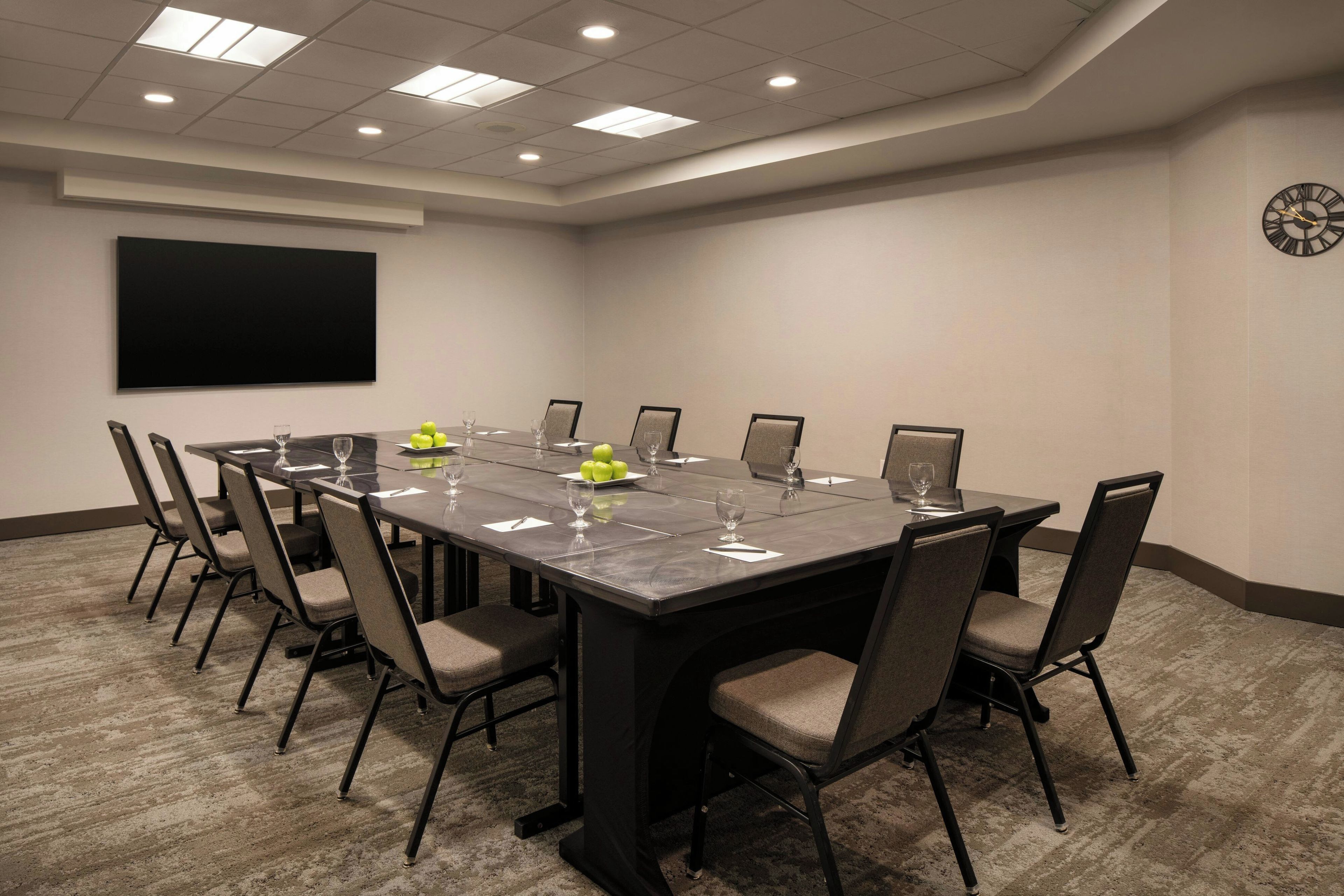A conference room with a long table, chairs, a projector screen, and a clock on the wall.
