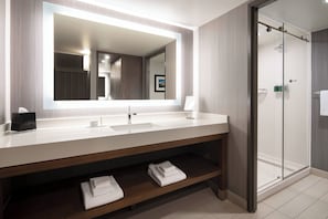 Un baño moderno con un espejo grande, un lavamanos y una cabina de ducha de vidrio.