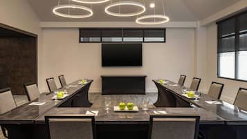 A conference room with a long table, chairs, a flat-screen TV, and pendant lighting.