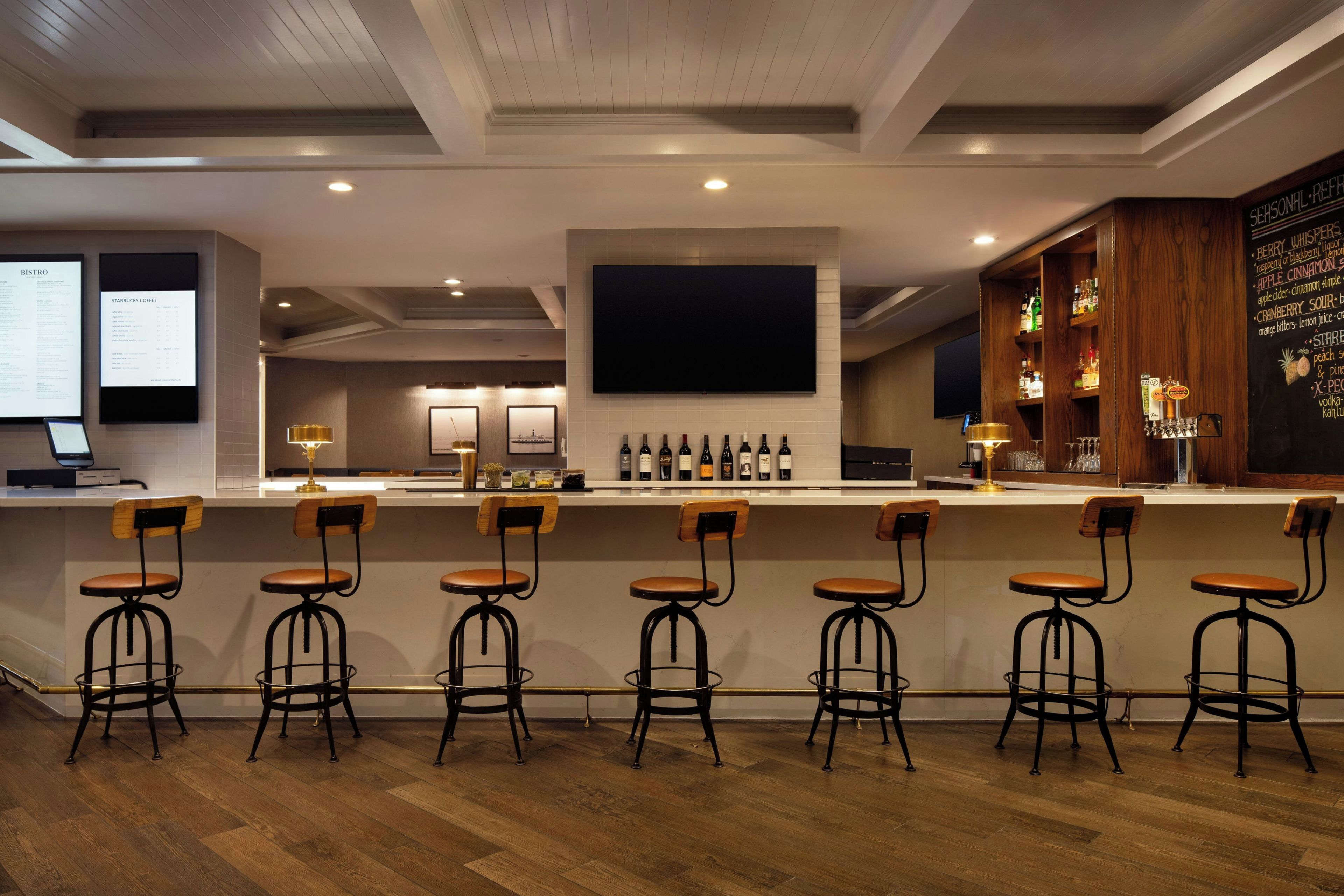 A bar area with wooden bar stools, a counter with a menu board, and a wall-mounted television.