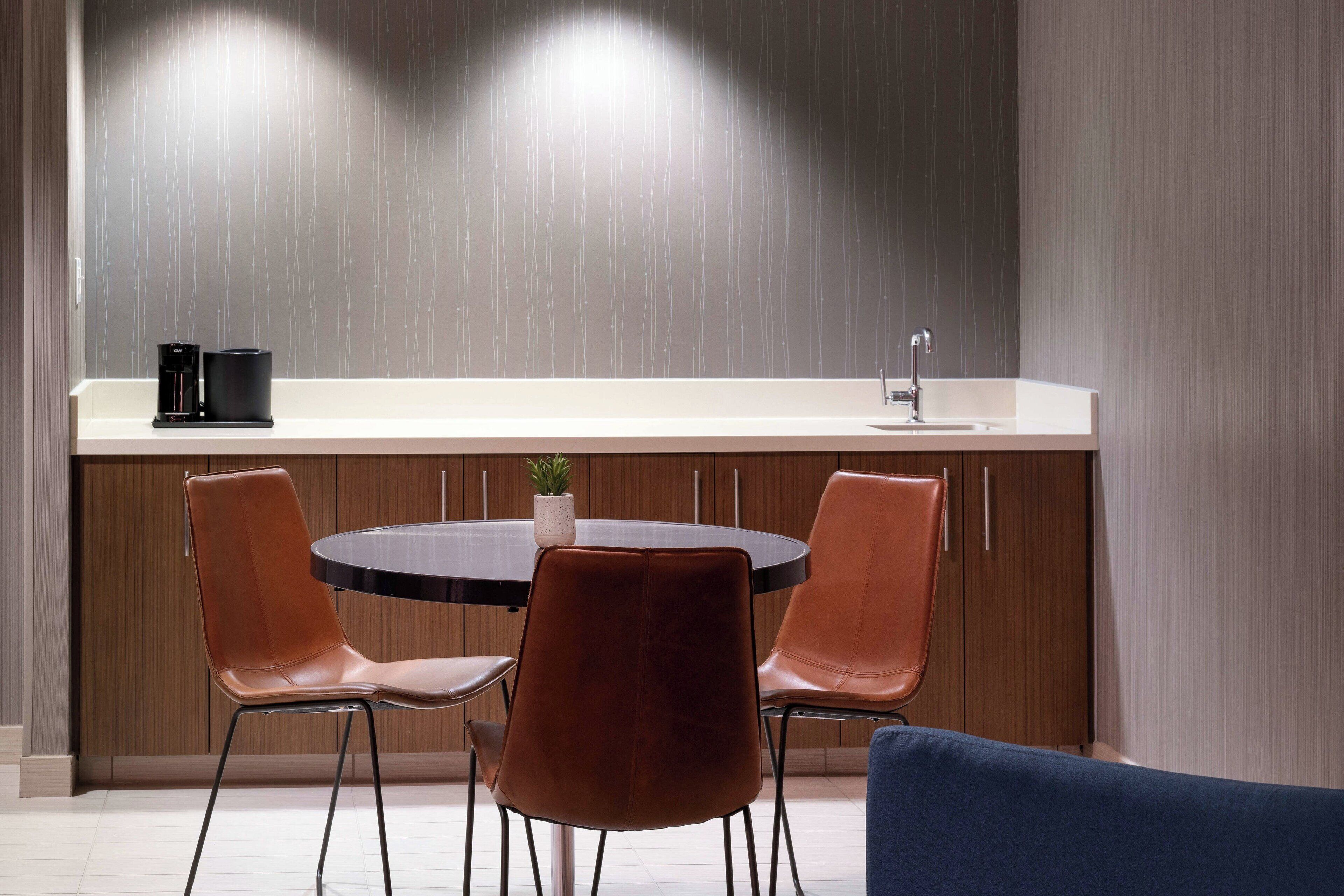 A modern kitchen with a round dining table, two chairs, a coffee maker, and a sink.