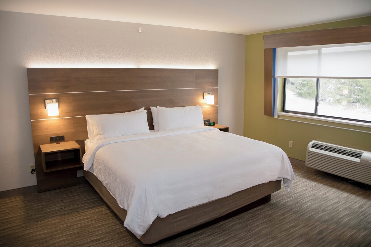 Una camera d'albergo moderna con un letto grande, lampade sui comodini, un comodino e una finestra con tende.