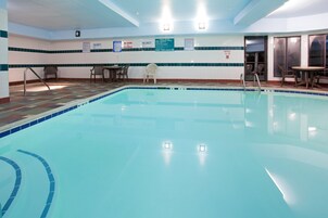 Una piscina interior con paredes de azulejos, algunas sillas y una mesa.