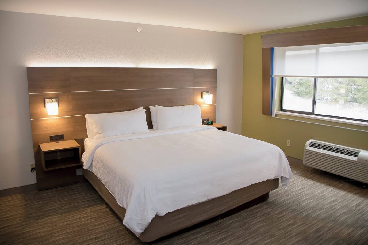 A modern hotel room with a large bed, bedside lamps, a nightstand, and a window with blinds.