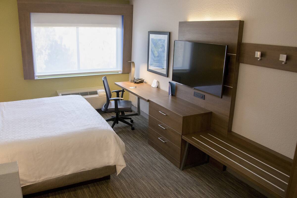 A hotel room with a bed, a desk, a chair, a flat-screen TV, and a window.