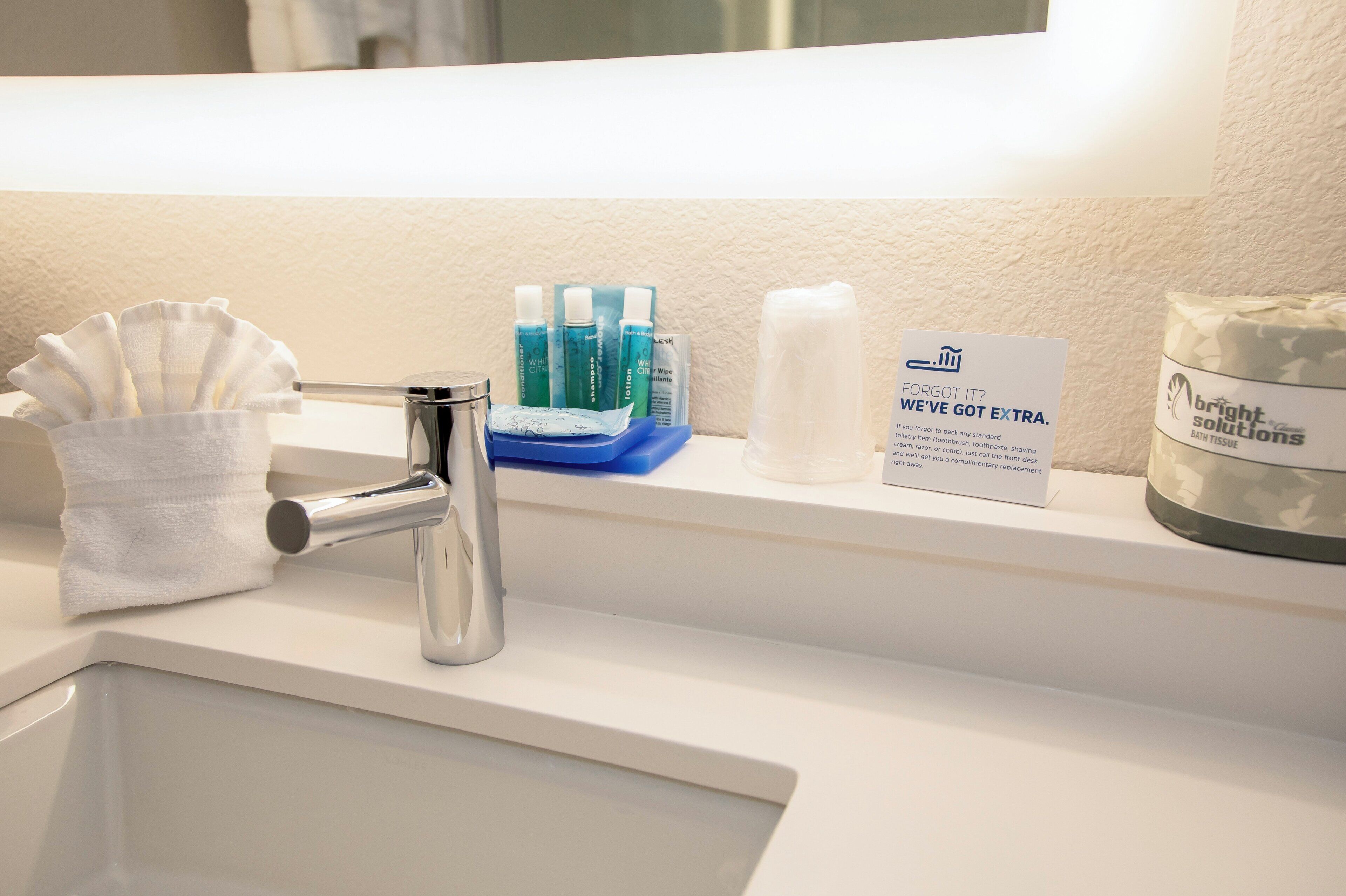 A hotel bathroom sink with toiletries including shampoo, conditioner, lotion, and bath tissue.