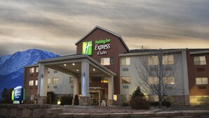 Un bâtiment de l’hôtel Holiday Inn Express & Suites, avec une façade en pierre, une entrée couverte et une montagne en arrière-plan.