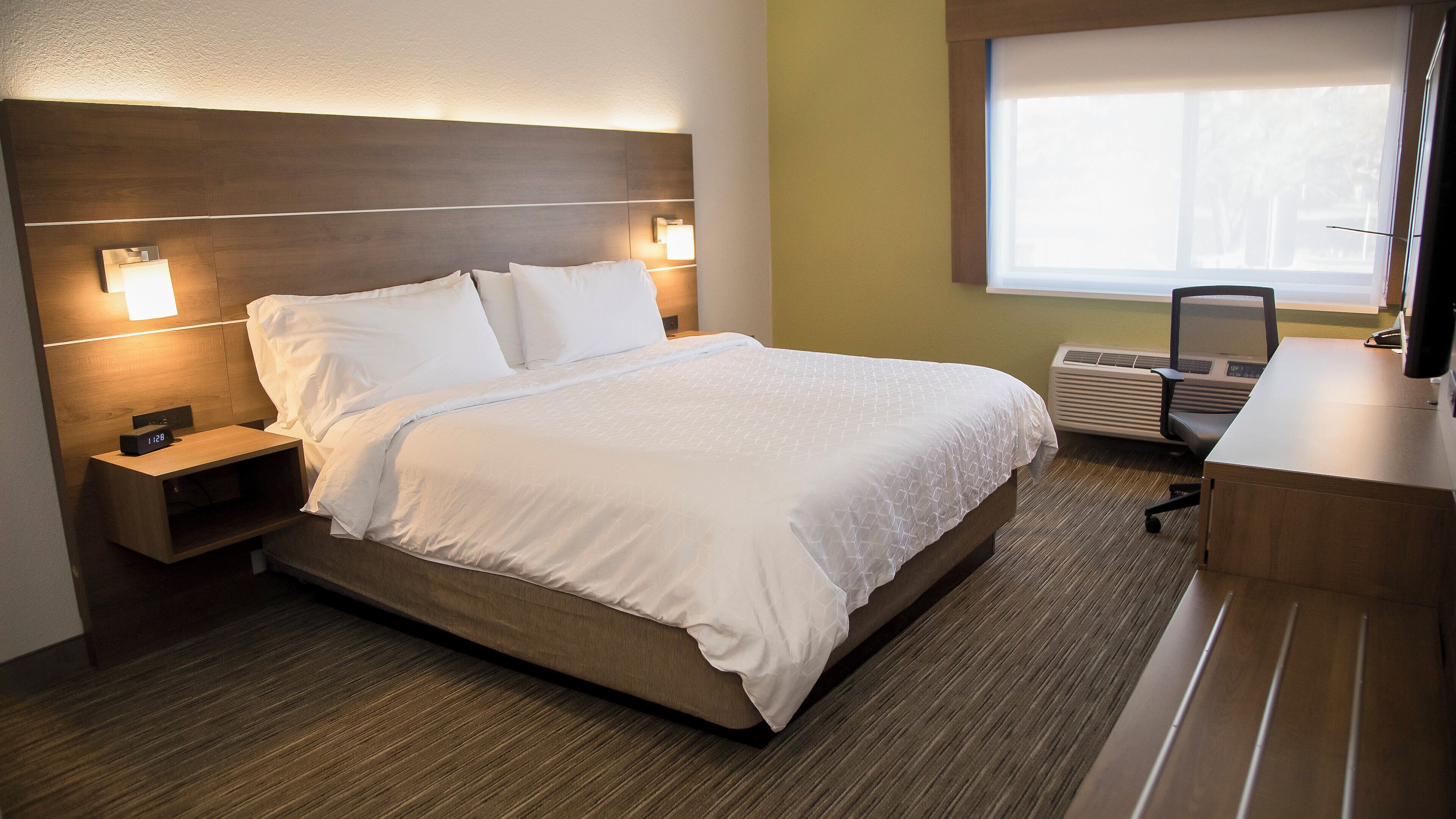 Una habitación de hotel con cama, mesita de noche, lámpara y un escritorio con silla.