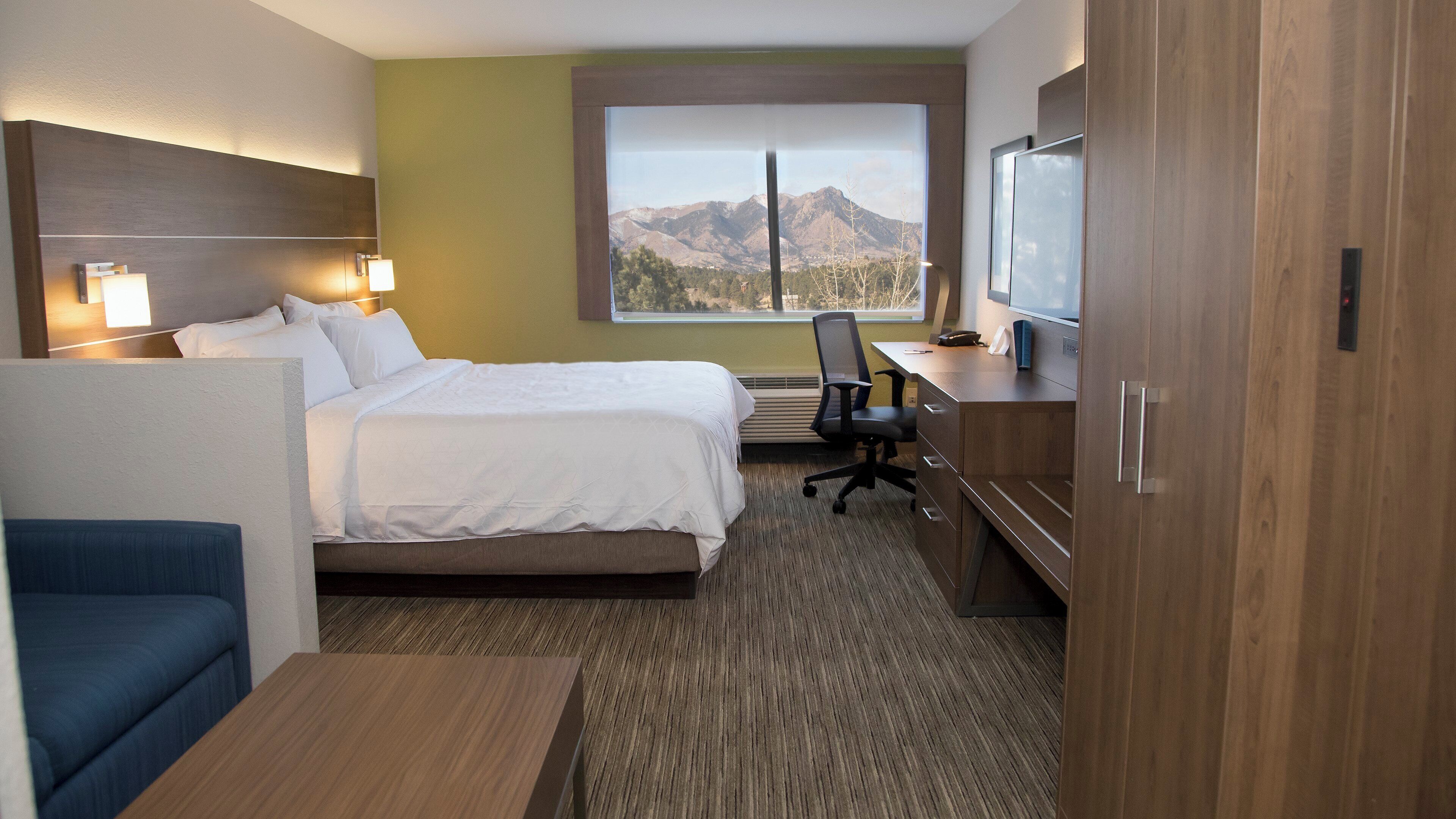 A hotel room with a bed, desk, chair, and a window with a mountain view.