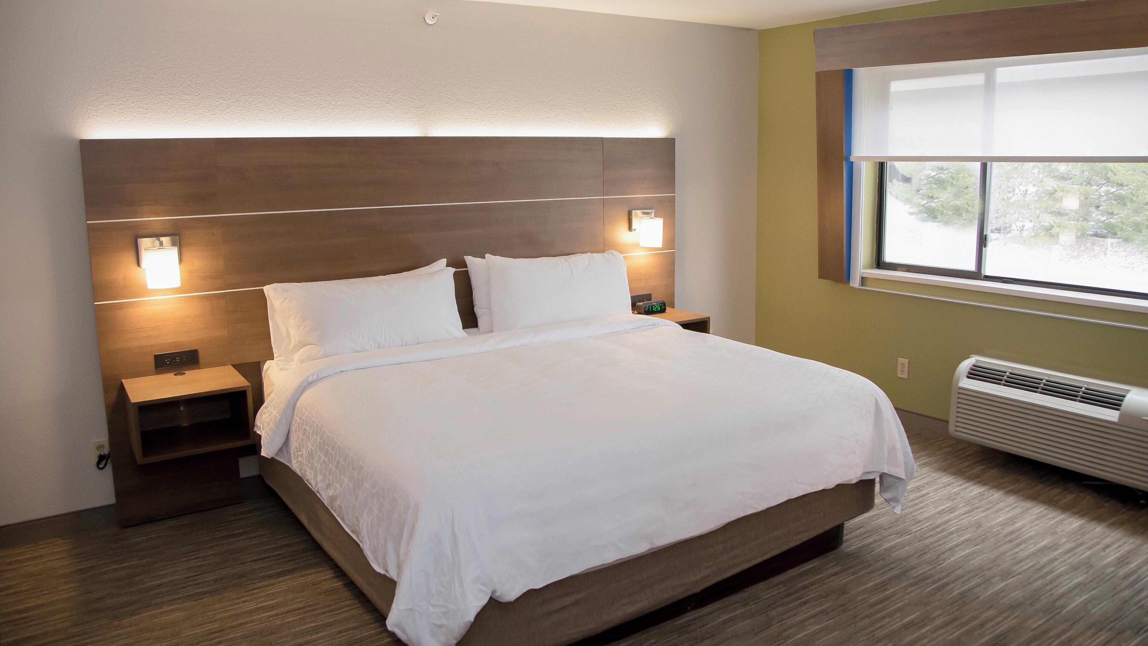 A neatly made bed with a headboard, bedside lamps, a nightstand, and a window with blinds.