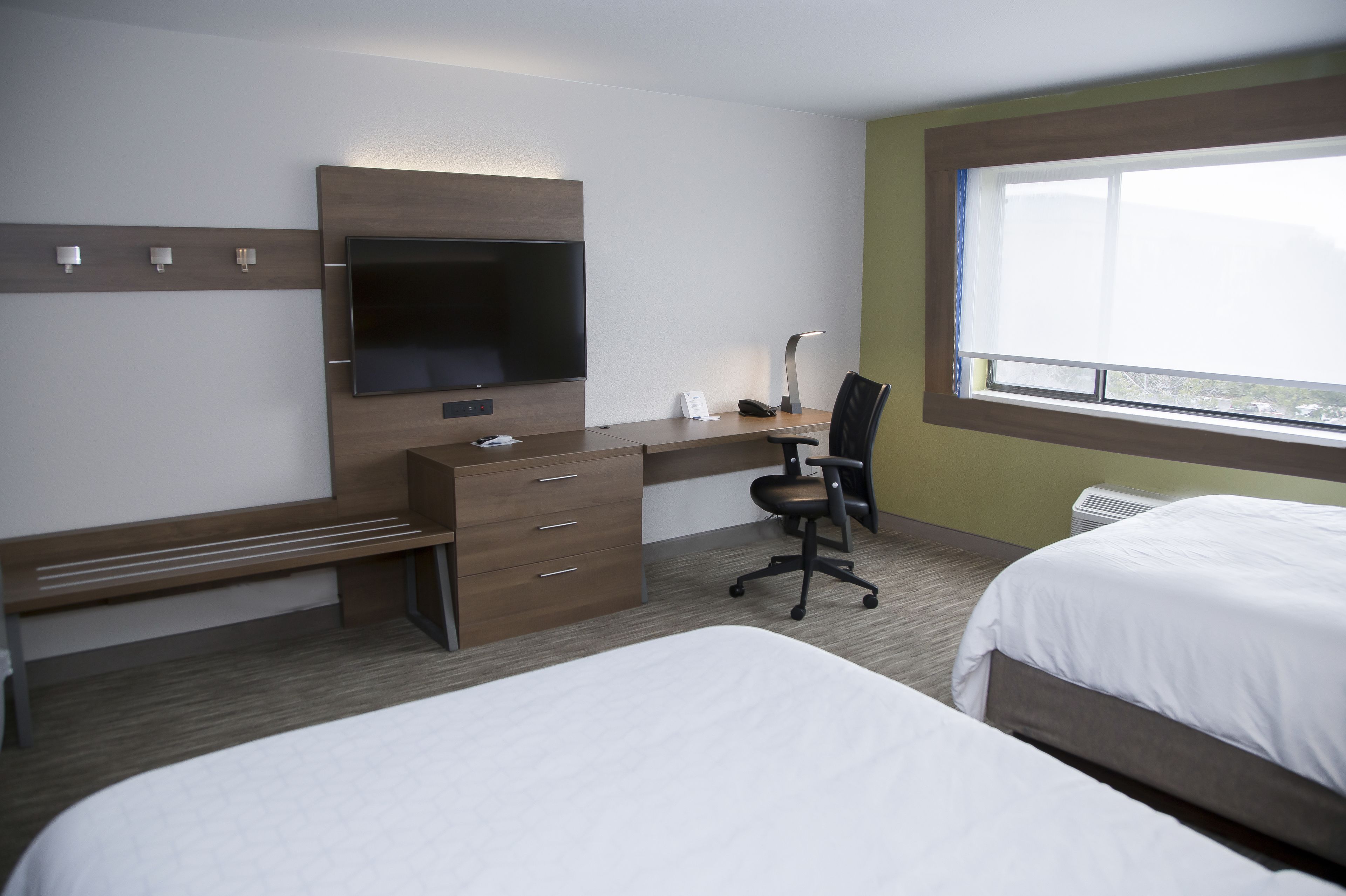 A hotel room with a bed, a desk with a chair, a television, and a window.