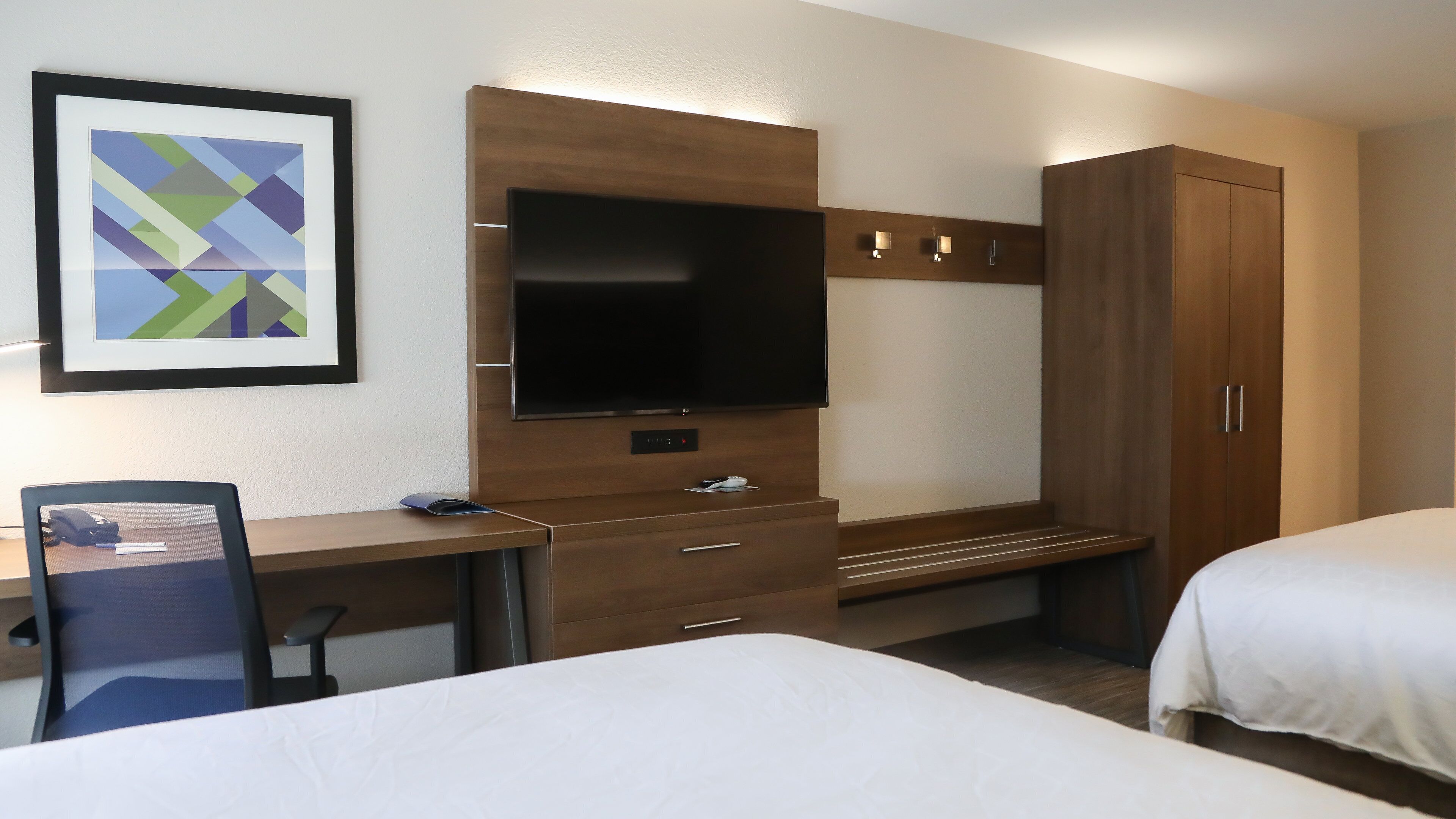 A hotel room with a bed, a desk with a chair, a television, and a wardrobe.