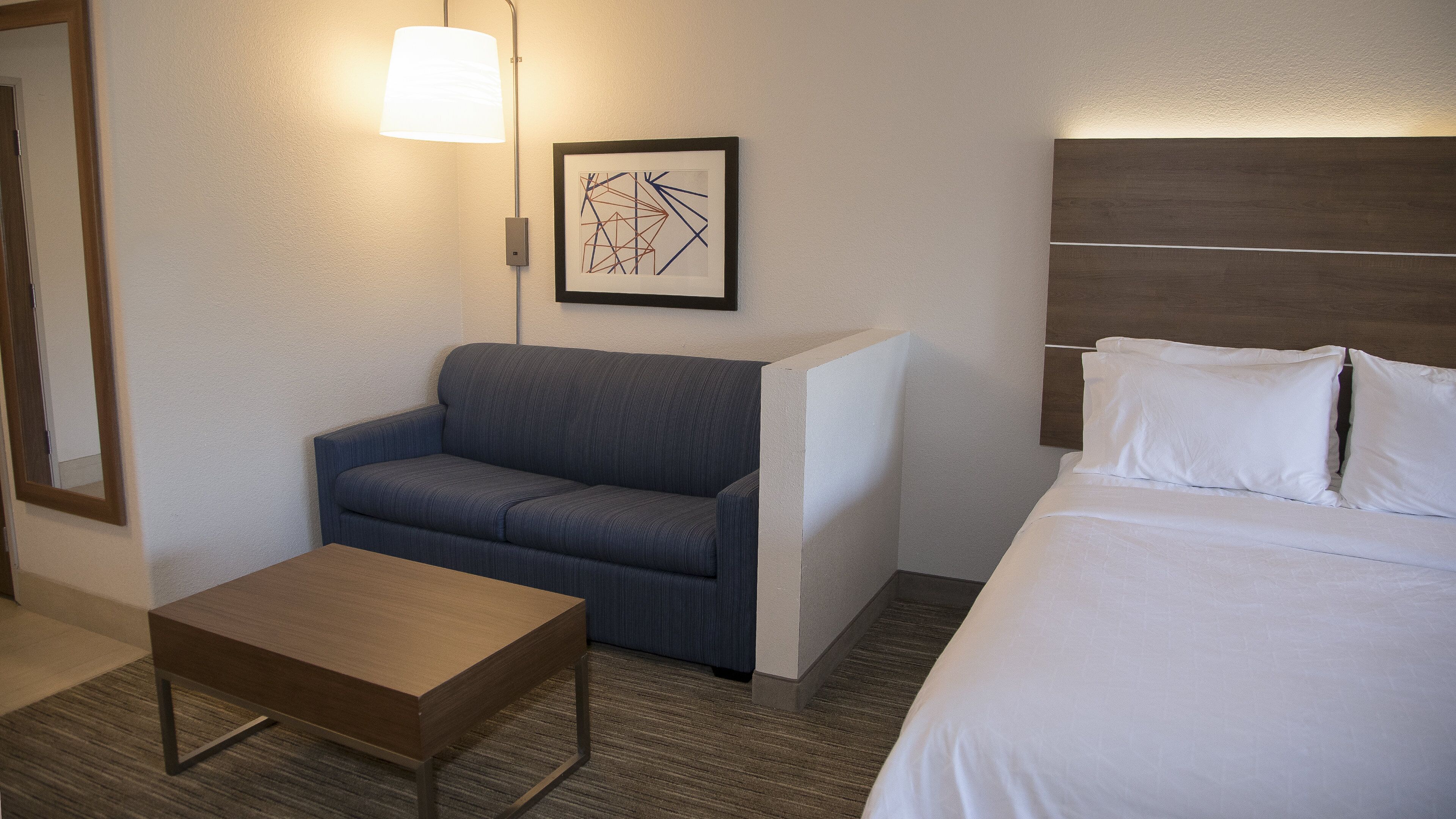 A hotel room with a bed, a sofa, a small table, and a lamp.