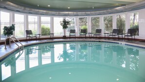 Une piscine intérieure à l’eau d’un bleu limpide, entourée de fenêtres et agrémentée de chaises et de plantes en pot.