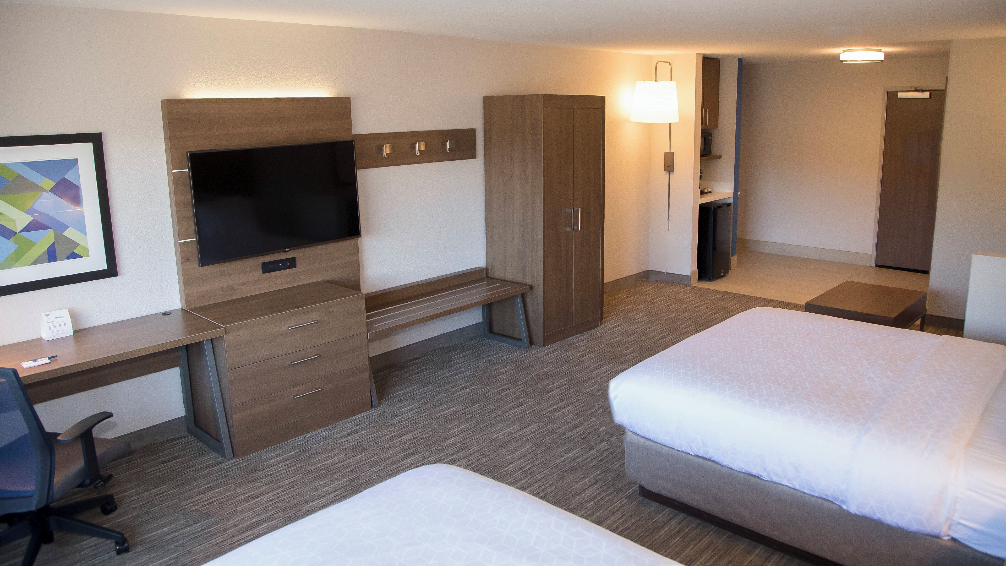 Habitación de hotel con cama, escritorio, silla, televisión, armario y mesita de noche.