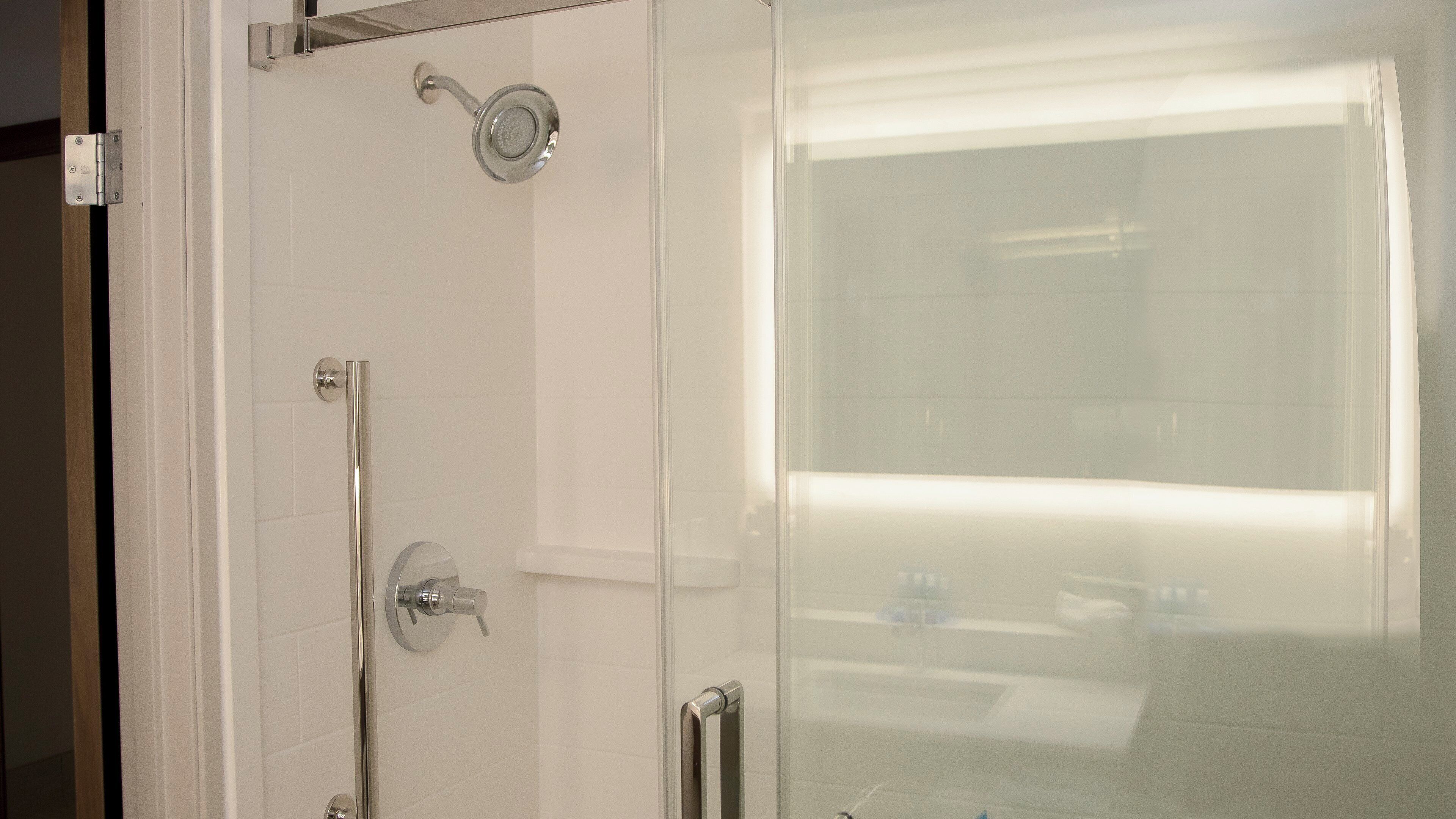 A glass-enclosed shower with a handheld showerhead and a handheld faucet.