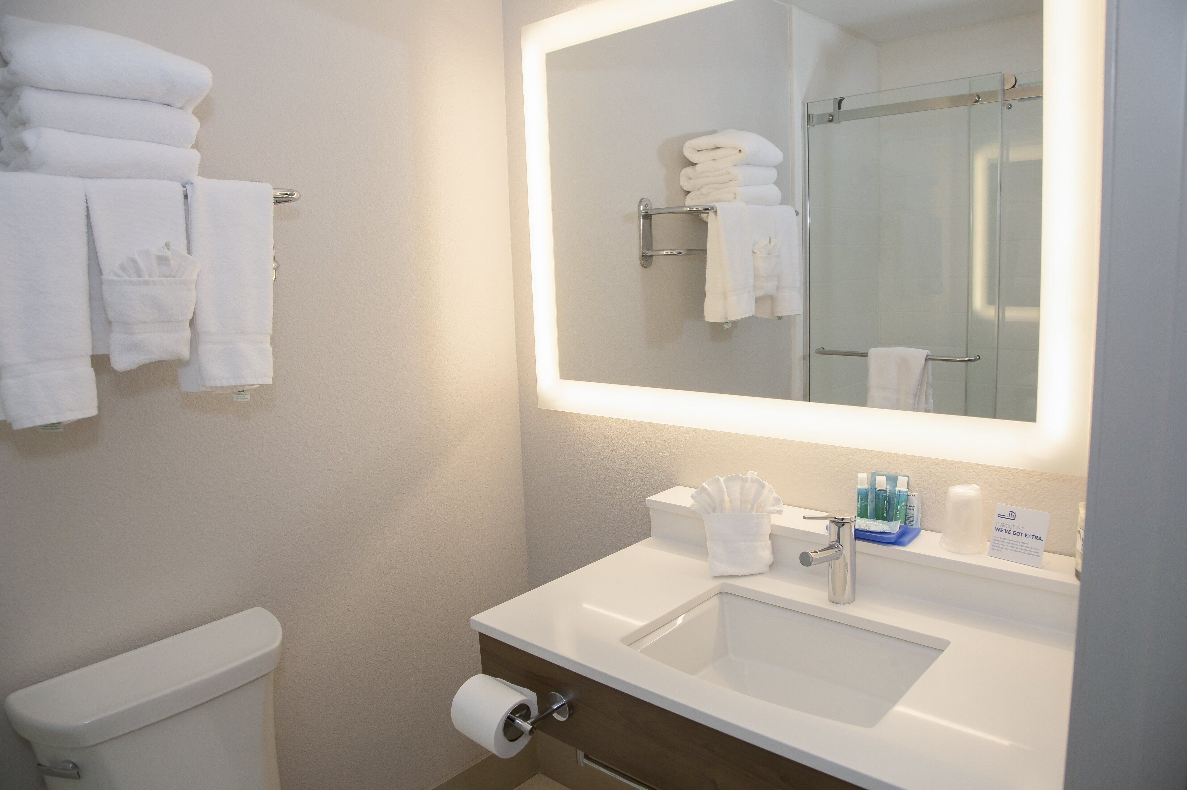 Un baño de hotel con inodoro, lavamanos y espejo con toallero.