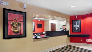 A hotel reception area with a red wall, a framed number '4', a reception desk, a mounted television, and an 'EXIT' sign. - Extended Stay America Suites Frederick Westview Dr (Frederick)