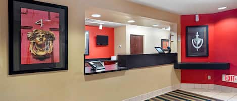 A hotel reception area with a red wall, a framed number '4', a reception desk, a mounted television, and an 'EXIT' sign.