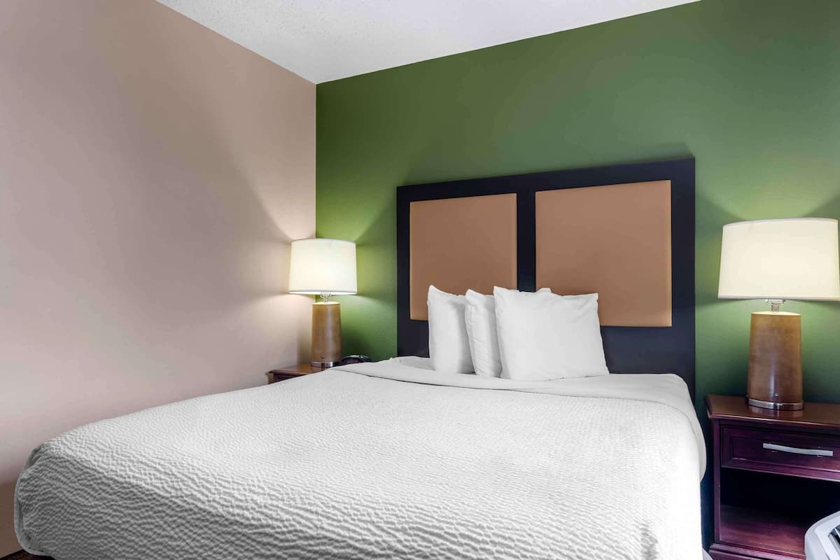 A hotel room with a bed, two bedside lamps, a nightstand, and a headboard with a large panel.