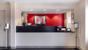 A reception desk with a red accent wall, a computer, and a phone. - Extended Stay America Select Suites Dallas Farmers Branch (Dallas)