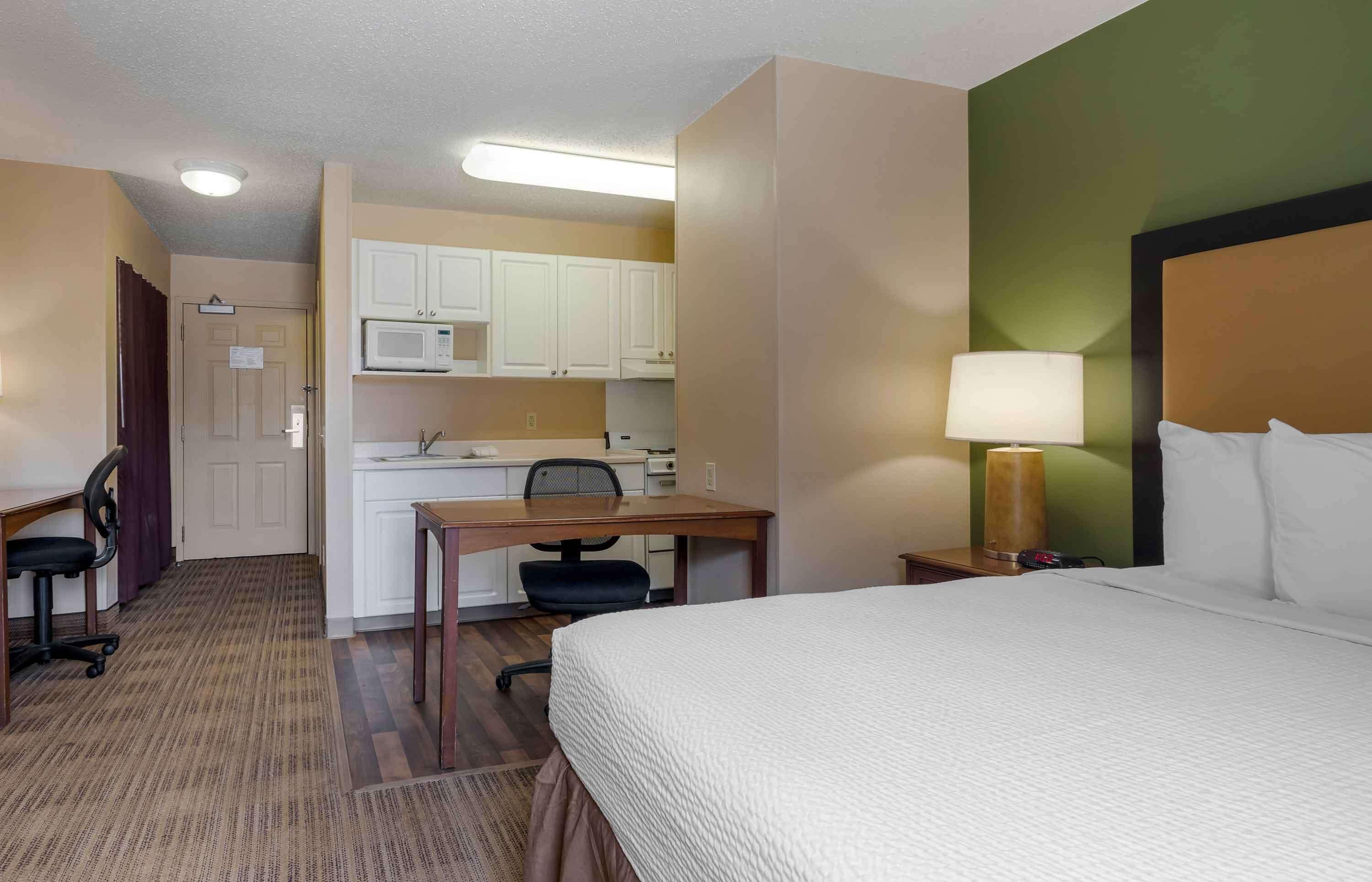 Een hotelkamer met een bed, bureau, stoel, kitchenette en een lamp.