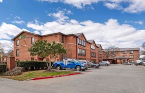 A brick building with a sign reading "Marriott Stay America." There are several vehicles parked in front, including a blue pickup truck and a silver car. - Extended Stay America Select Suites Dallas Farmers Branch (Dallas)