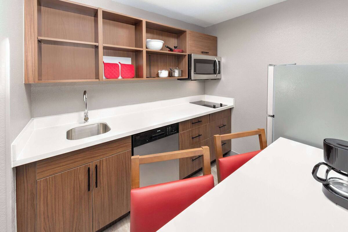 A compact kitchen with wooden cabinets, a built-in microwave, a refrigerator, and a white countertop.