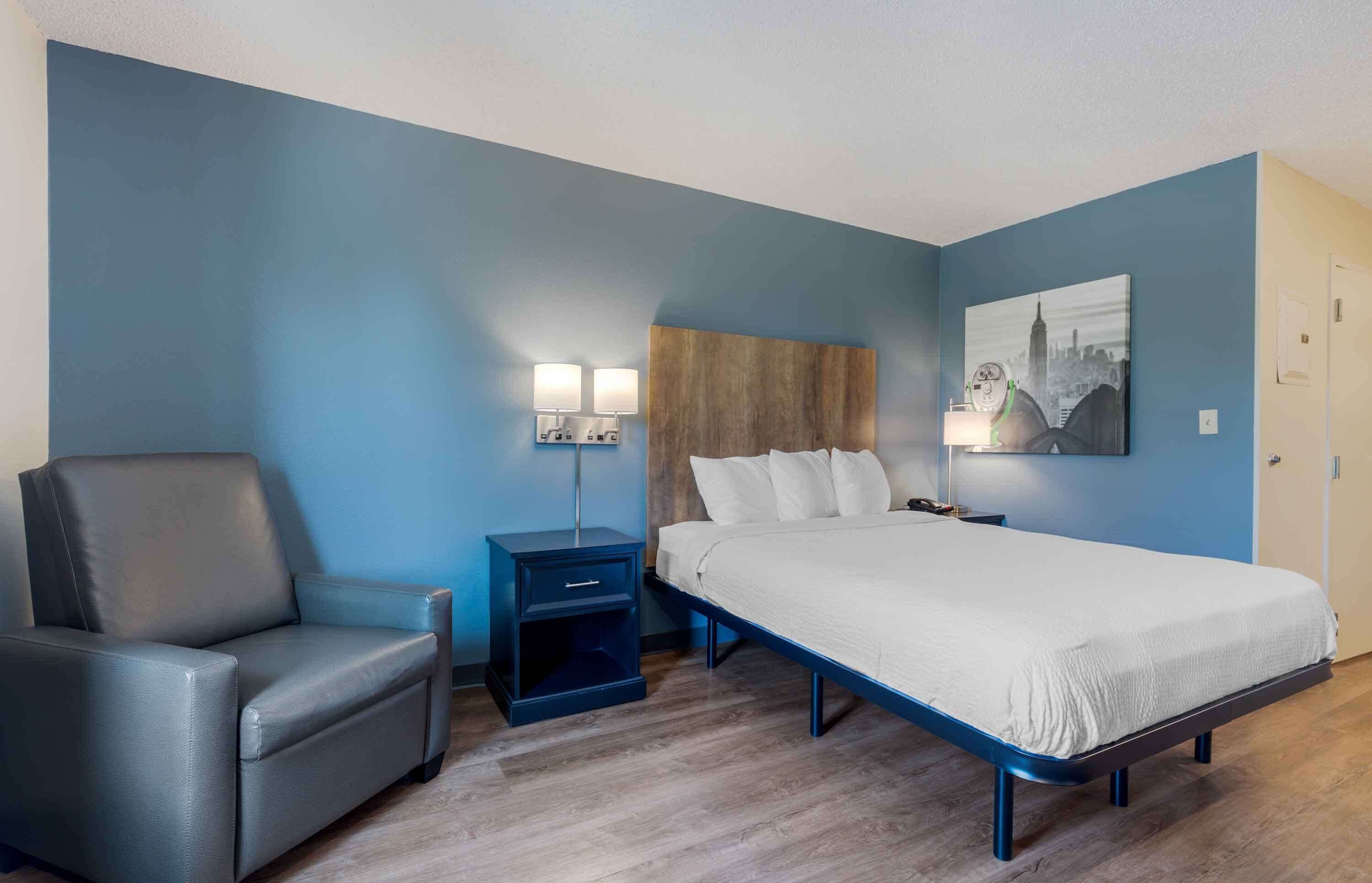 A bedroom with a bed, a chair, a nightstand, and a wall-mounted lamp.