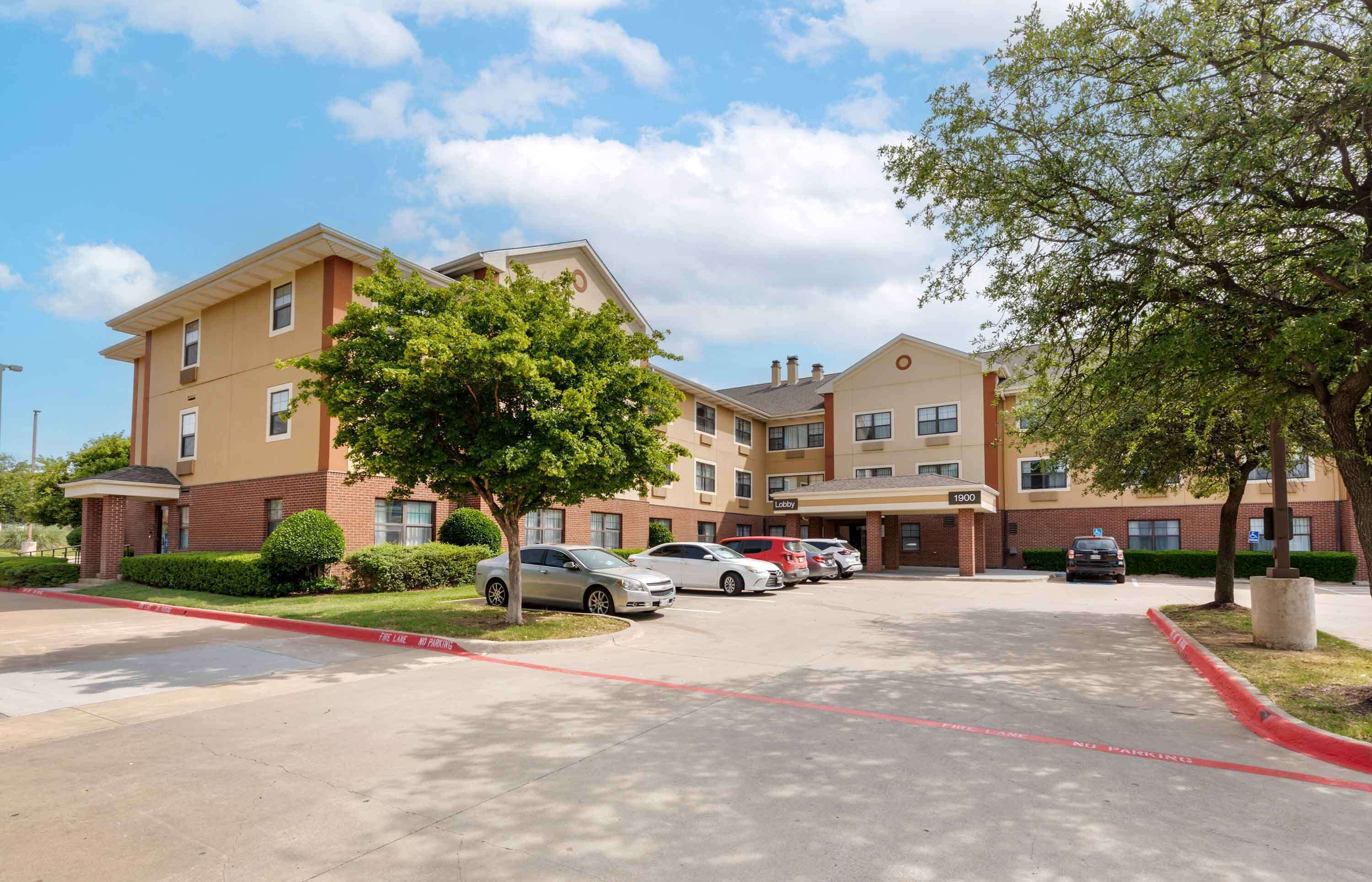 A multi-story hotel with a parking lot, a lobby, and a tree-lined driveway.