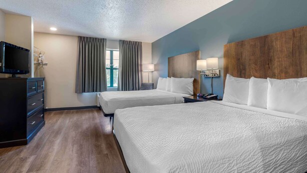 Een hotelkamer met twee bedden, een televisie, een dressoir en een raam met gordijnen.