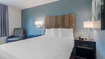 A hotel room with a large bed, a chair, a nightstand with a lamp, and a wall-mounted picture.
