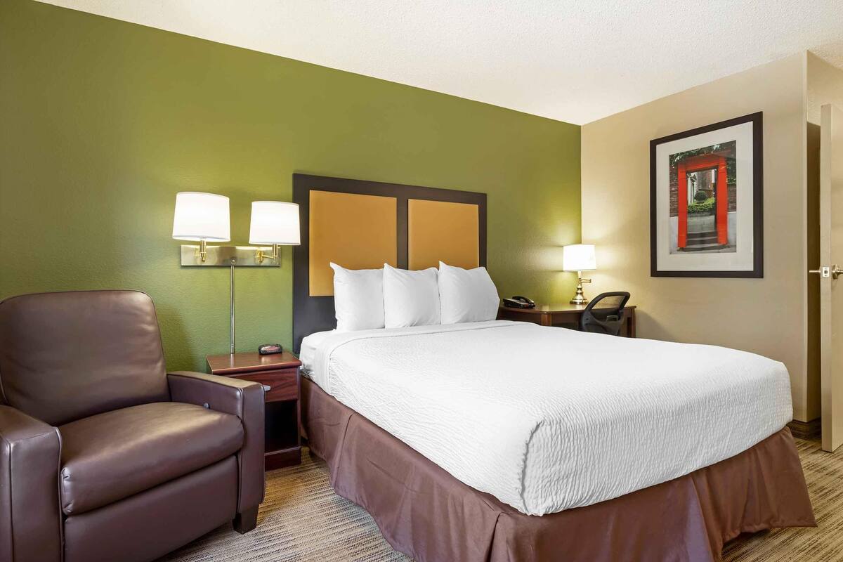A hotel room with a large bed, a brown leather chair, two bedside lamps, and a framed picture on the wall.