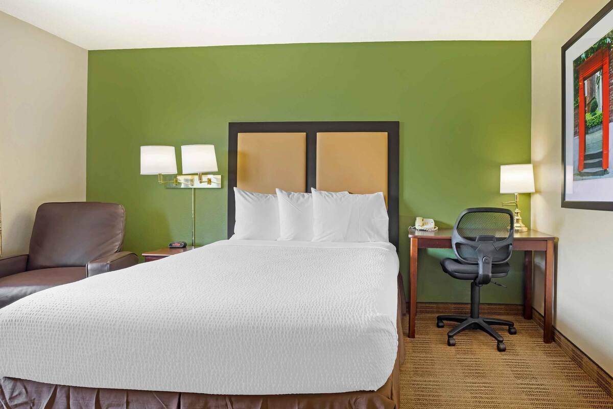 A hotel room with a large bed, a desk with a chair, two bedside lamps, and a framed picture on the wall.