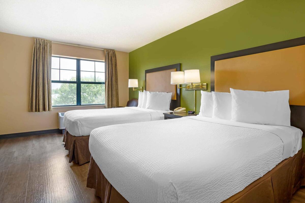 A hotel room with two beds, a large window with curtains, and a green wall.