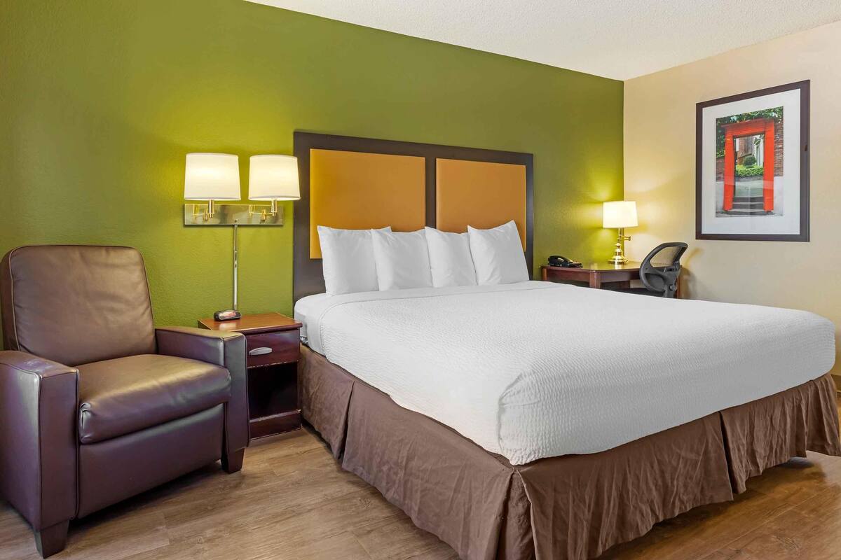 A hotel room with a large bed, a brown leather chair, two bedside tables with lamps, and a framed picture on the wall.